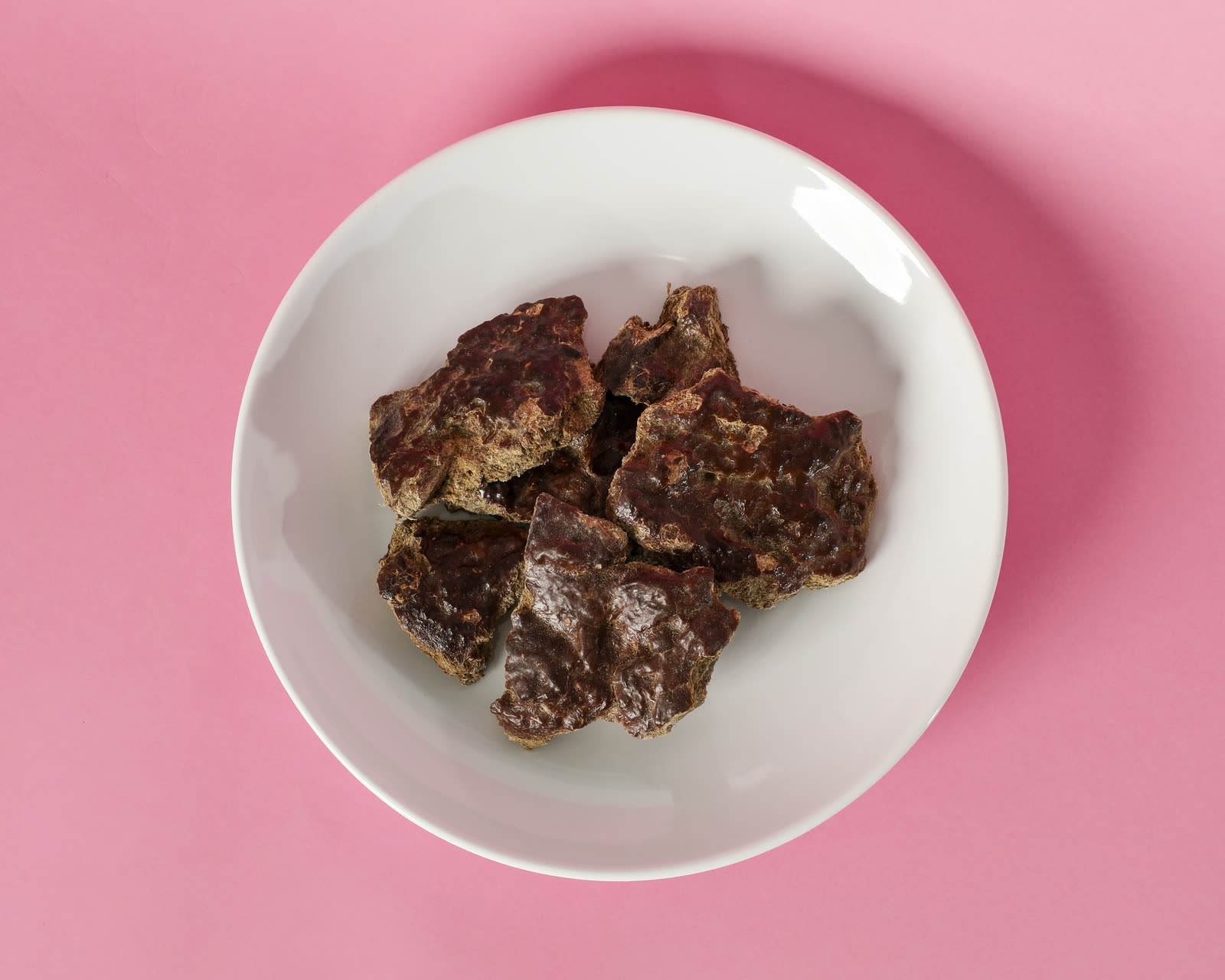 Bison liver freeze-dried treats on a white plate, shot overhead on a rose seamless background