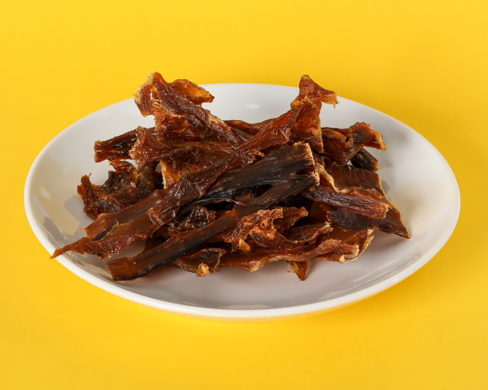 Water buffalo meat strips on a white plate on a yellow seamless background