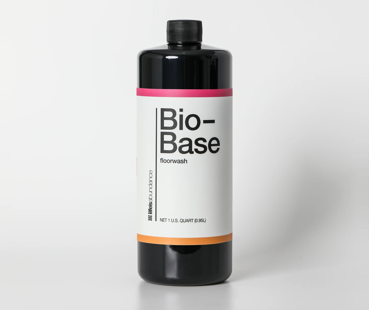 Bio-Base floorwash concentrate, black one-quart bottle with the pink and orange banded label, straight on against a pale studio seamless