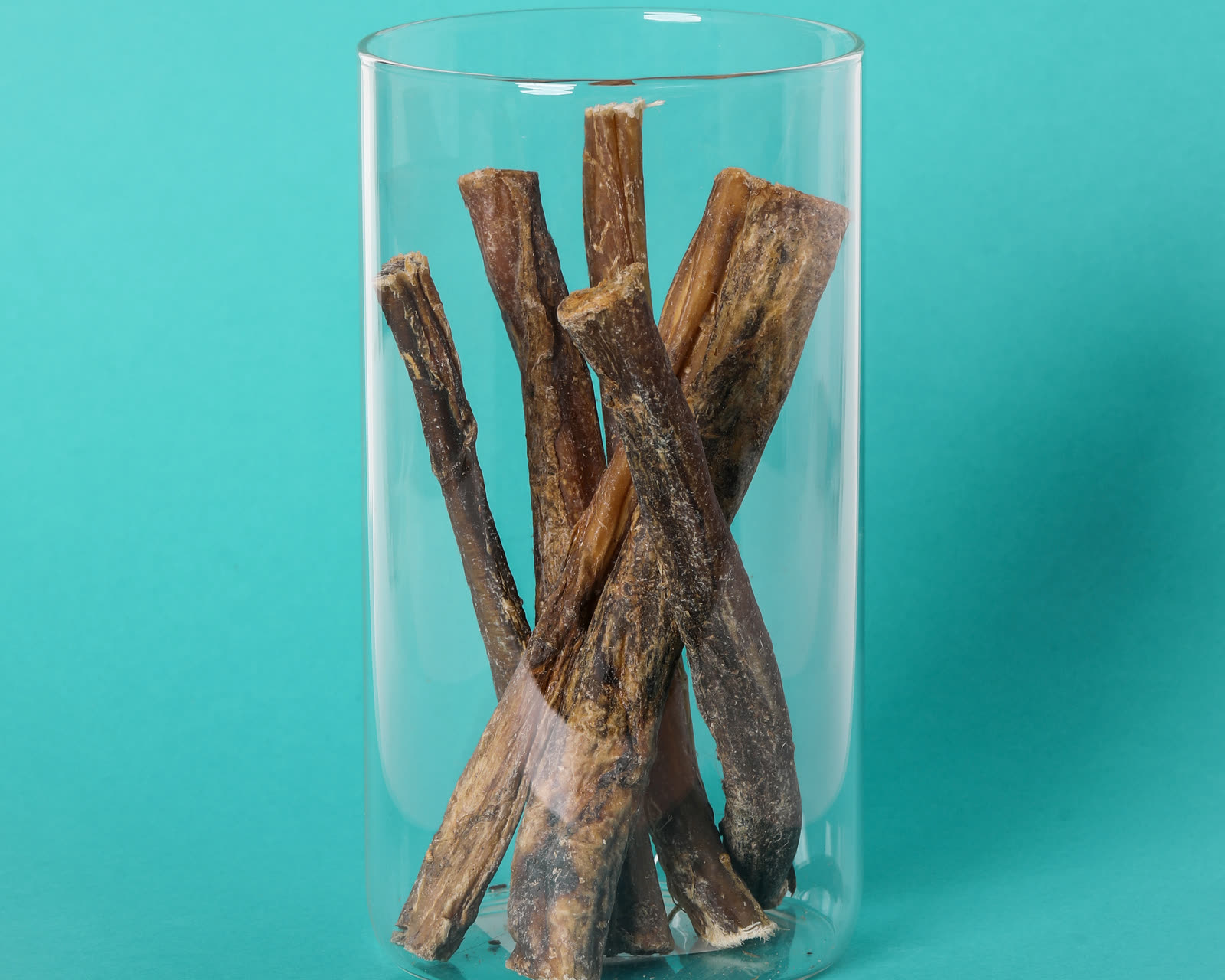 Six 6-inch water buffalo bully sticks standing in a glass jar on a teal background
