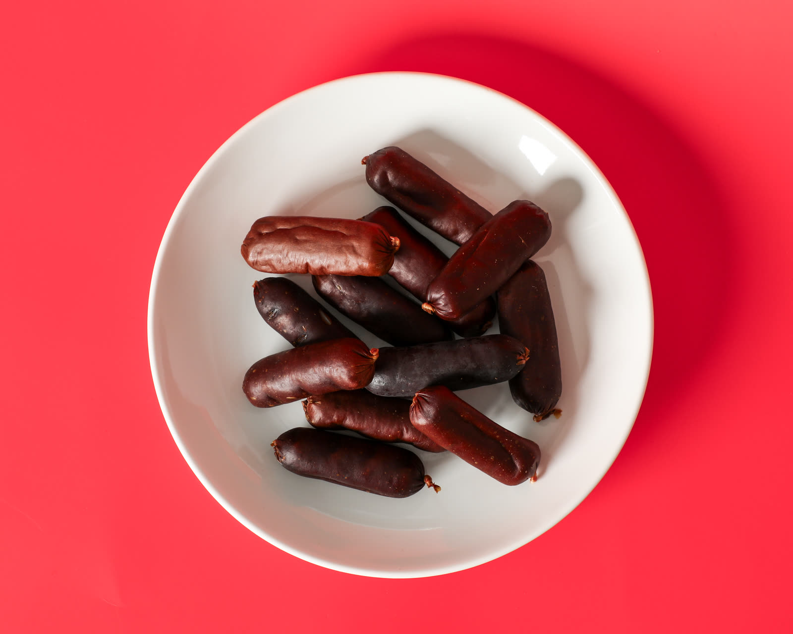 Pork & apple recipe sausage treats in a white bowl, shot overhead on a red seamless background