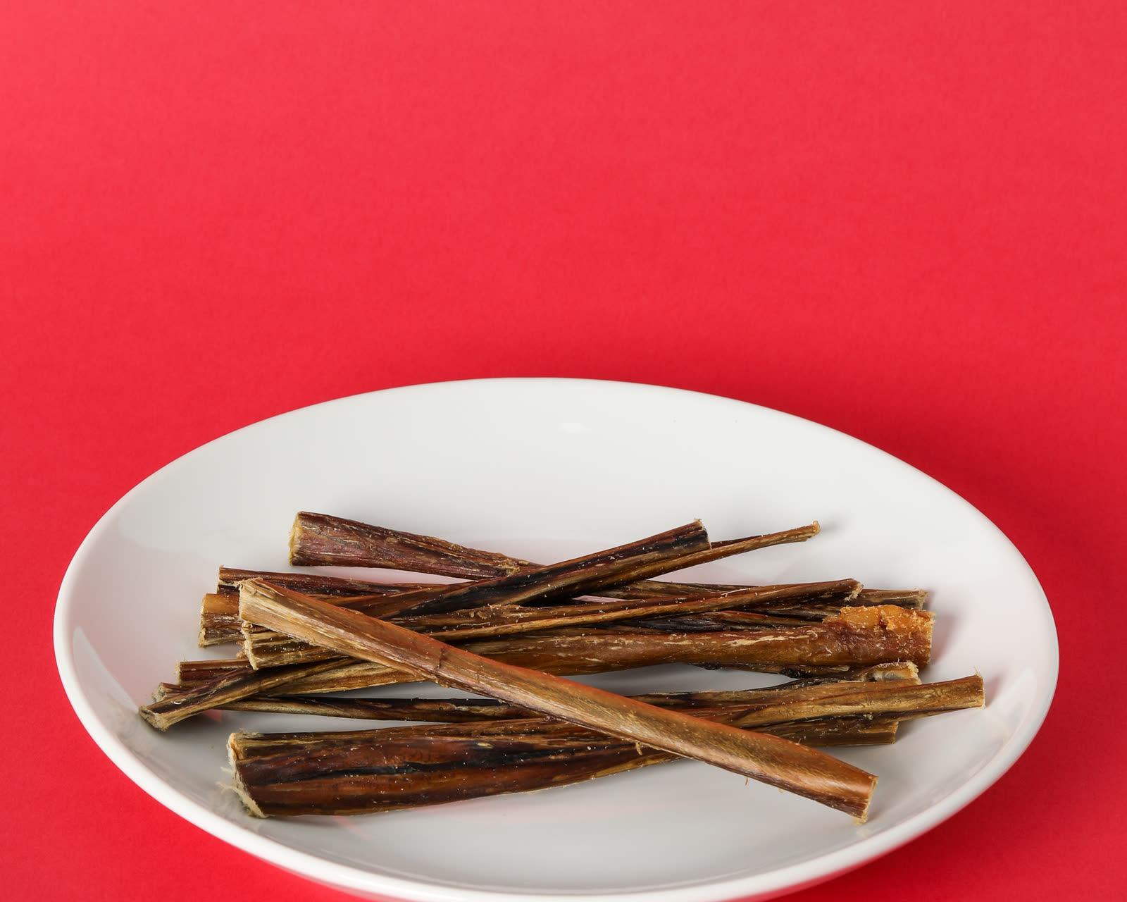Pork bully sticks piled on a white plate on a red background