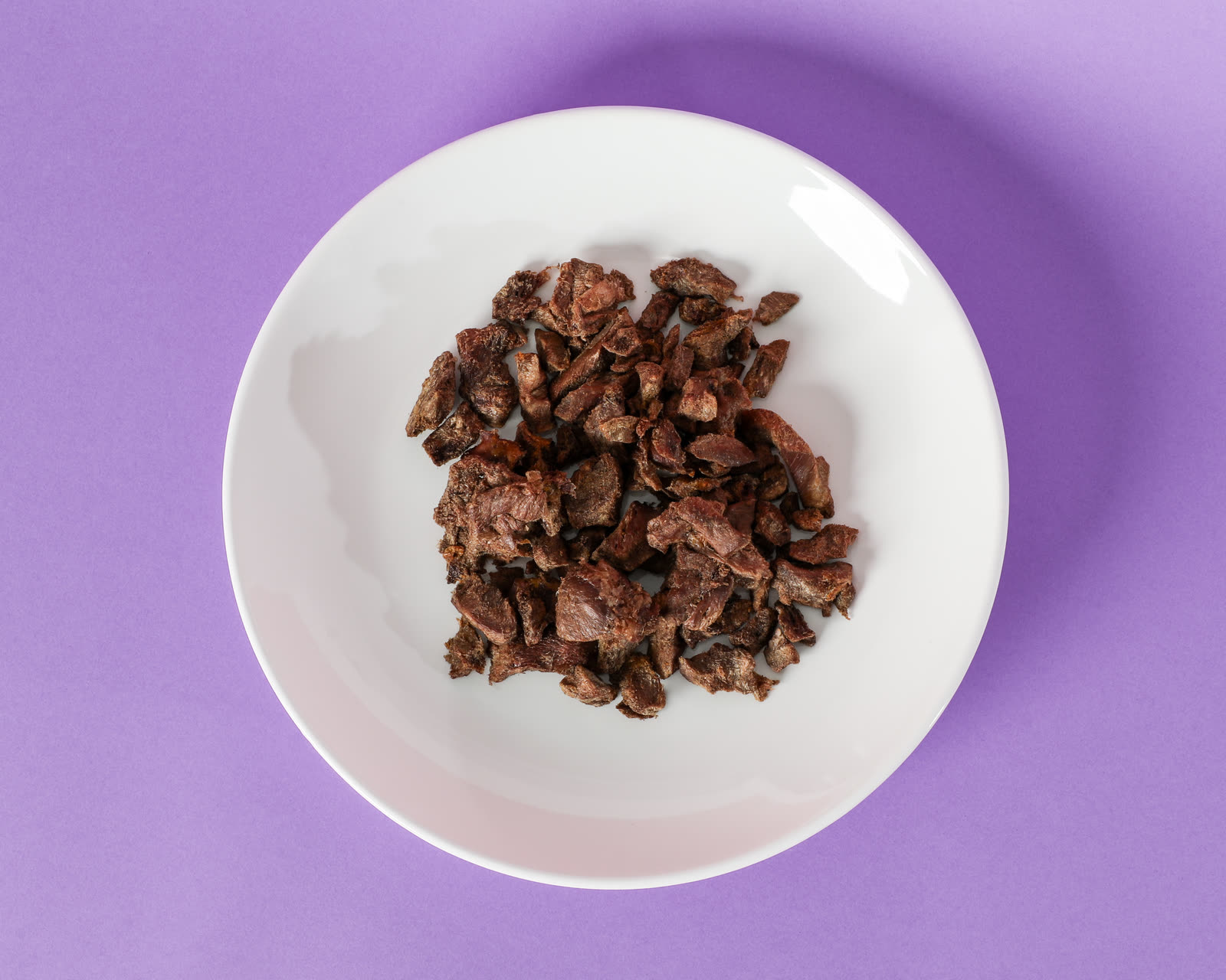 Turkey Heart Petites freeze-dried dog treats on a white plate against a purple background