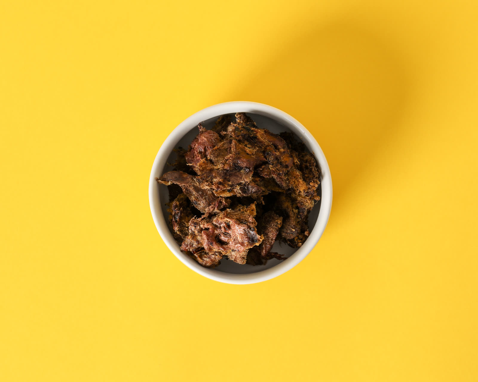 Turkey Hearts freeze-dried cat treats in a white bowl on a yellow background, photographed from above